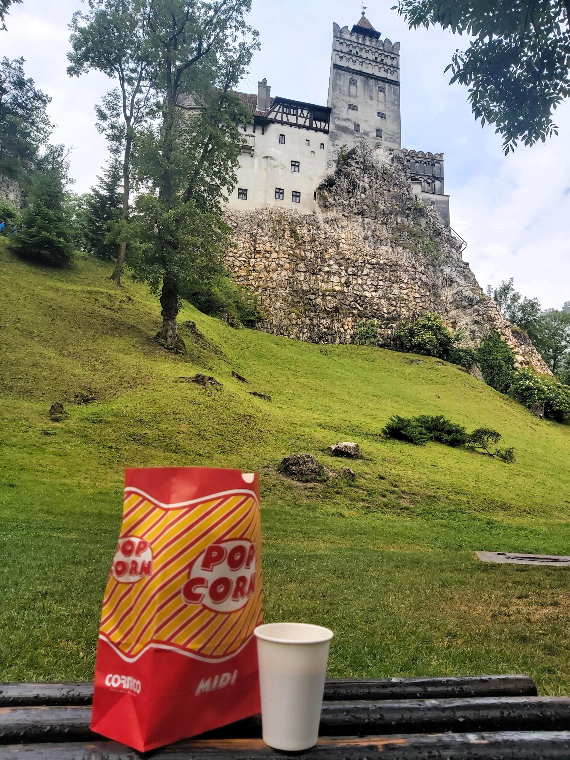 A view of Bran Castle, Romania, with a red and yellow popcorn bag and cup of coffee in front.