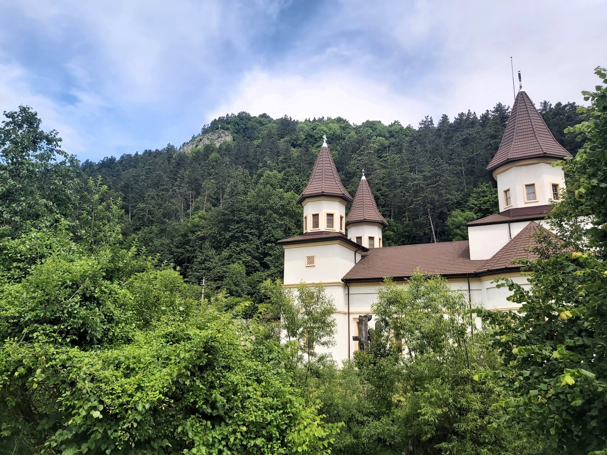 A white church poking out from behind green trees in Bran, Romania