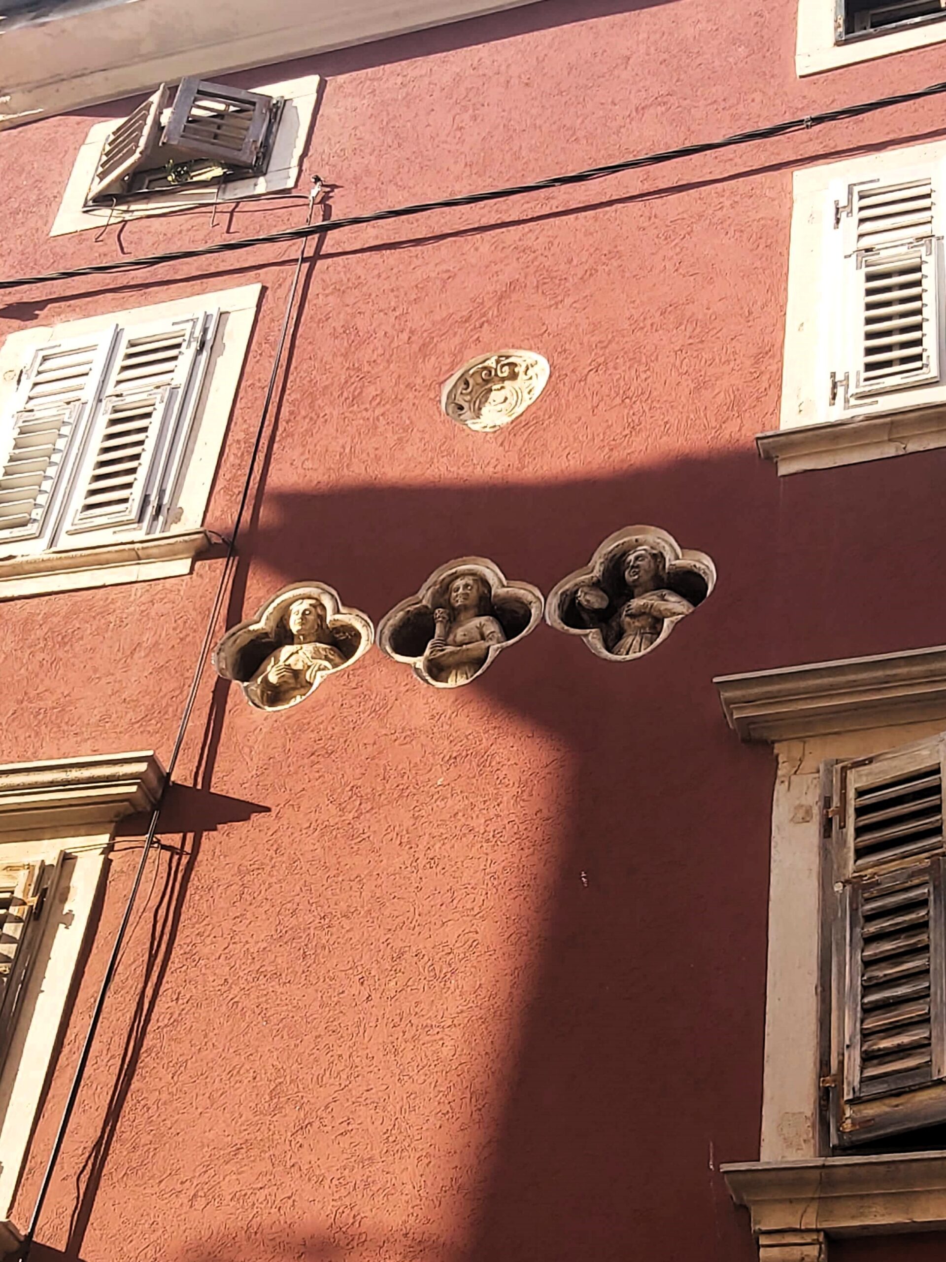 3 white statuettes embedded in a red walled building, Pula, Croatia