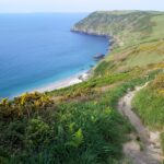 A far reaching view of Lantic bay with the path and signpost on the cliff, Cornwall, England