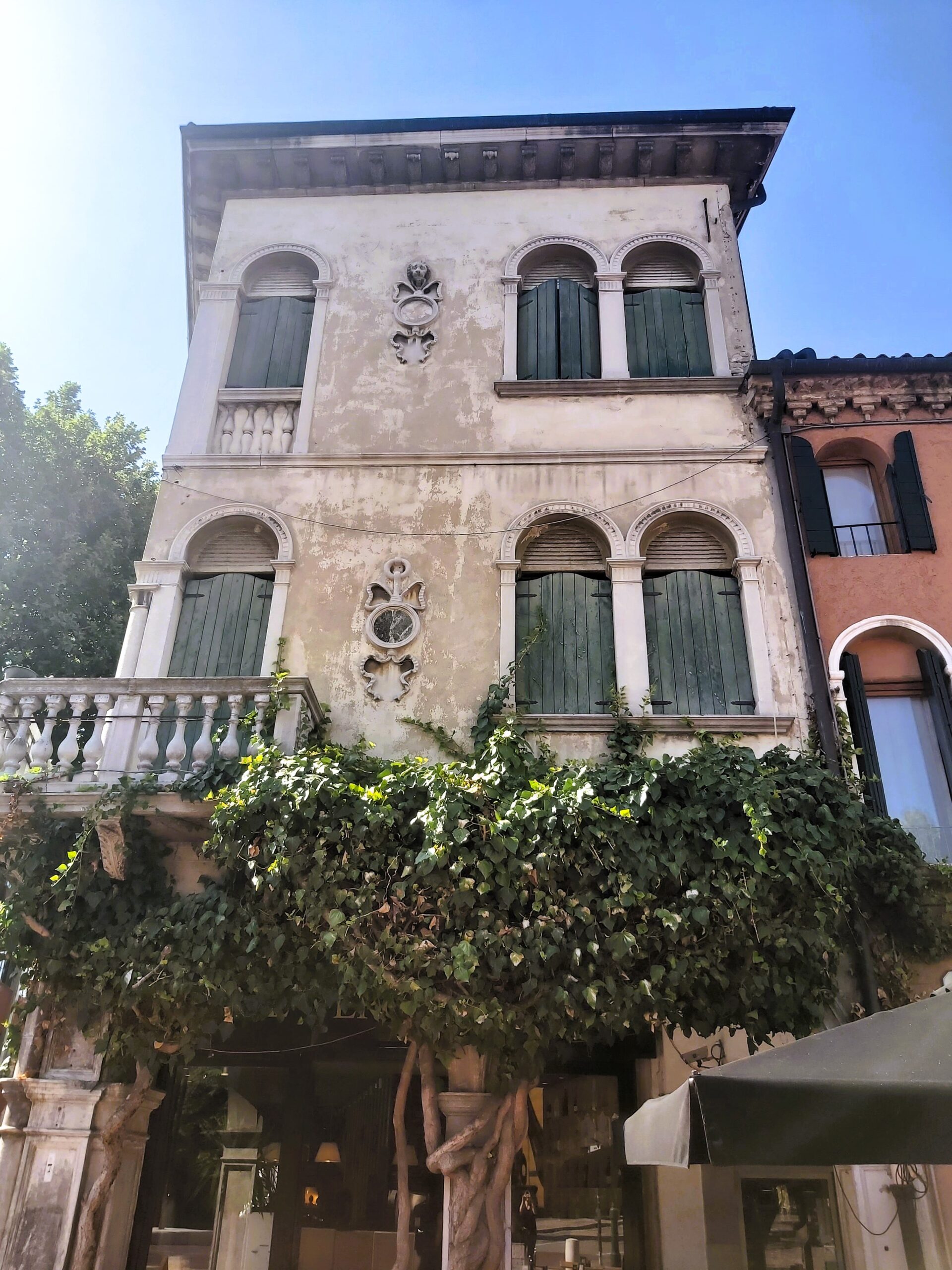 An old building with green shutters and arched windows. A pretty scene with foliage in Mestre, Italy