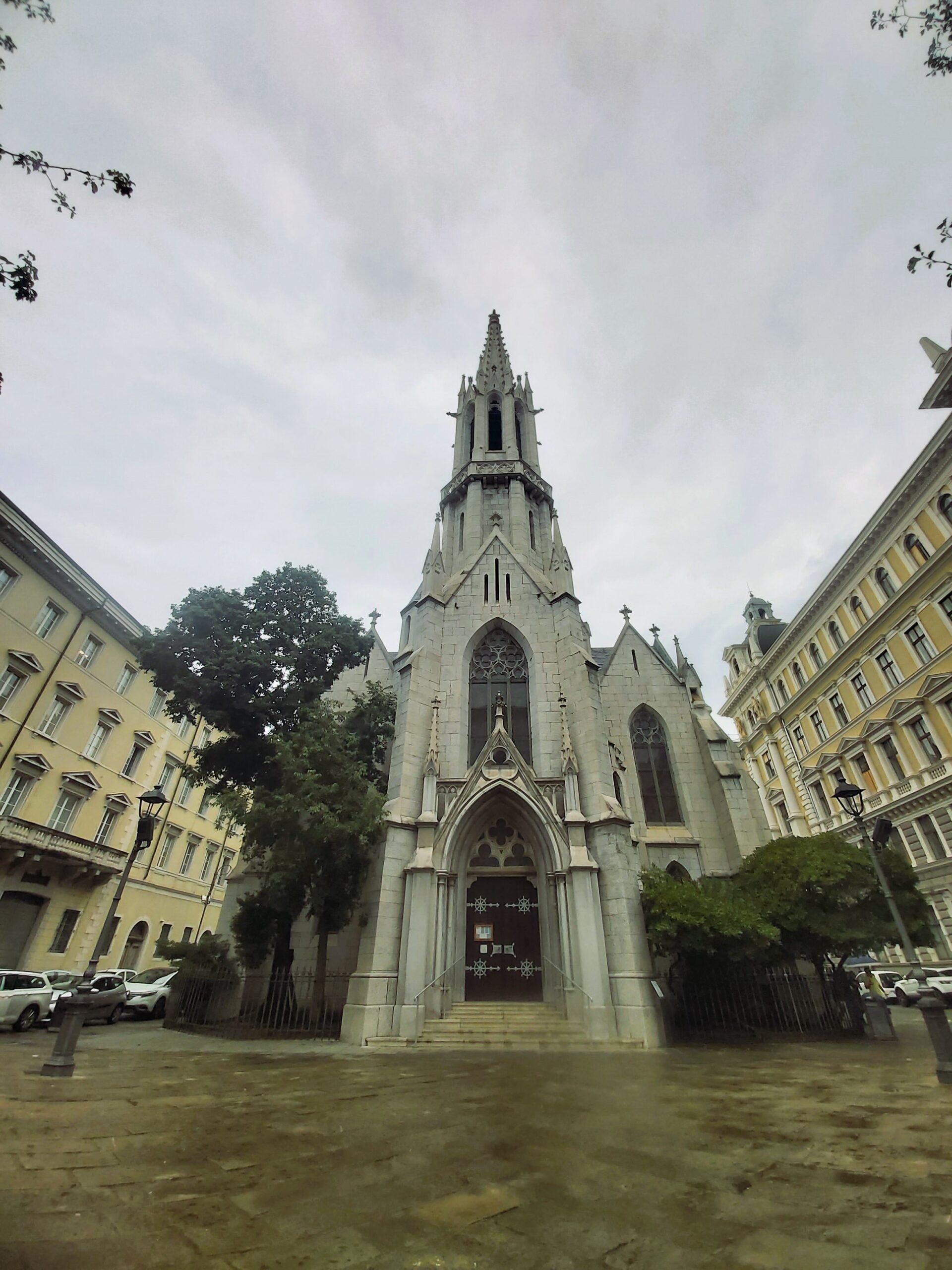 A grey church between brighter buildings in Trieste, Italy