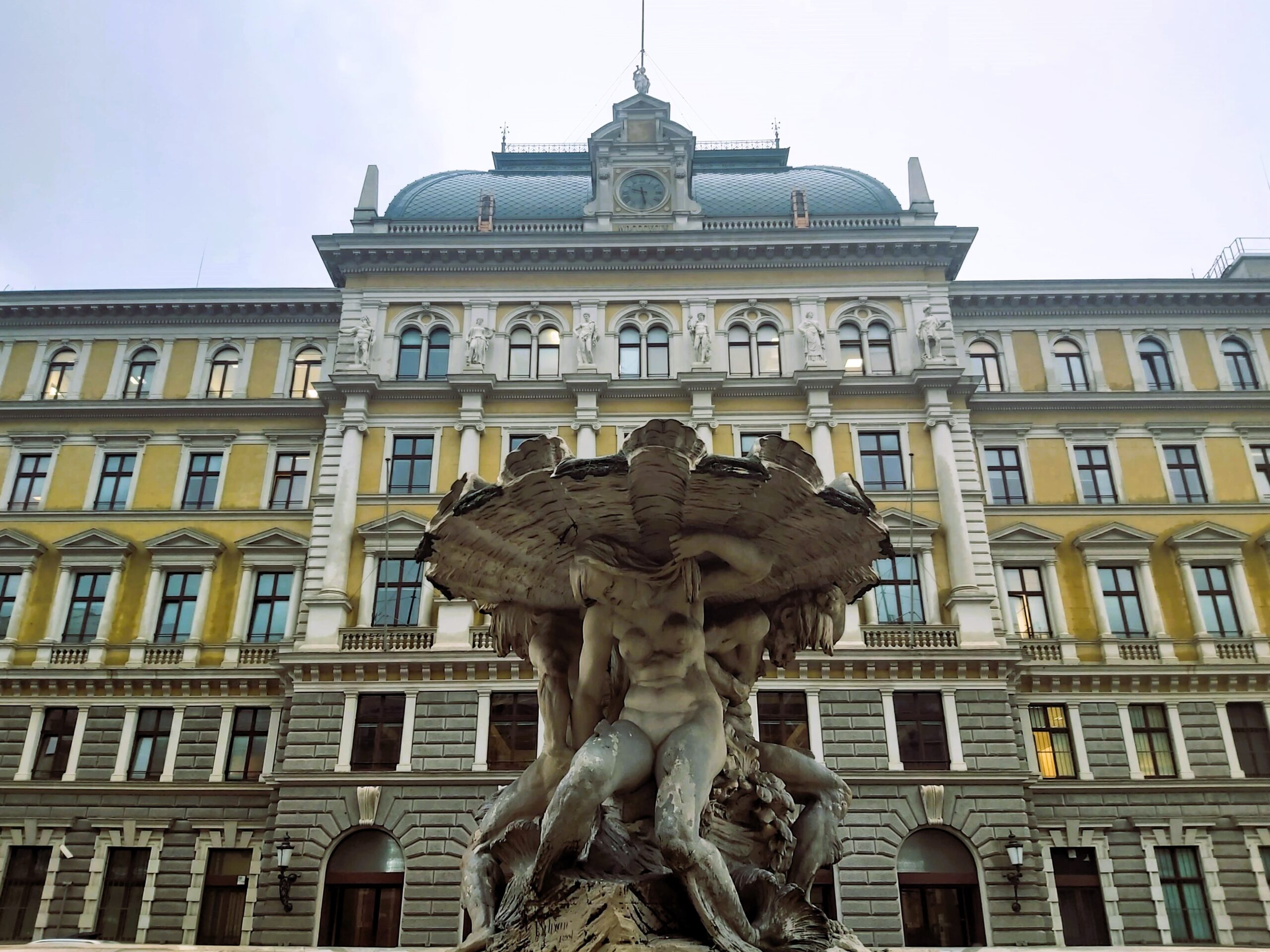 A naked woman statue on a fountain in front of a yellow building in Trieste, Italy