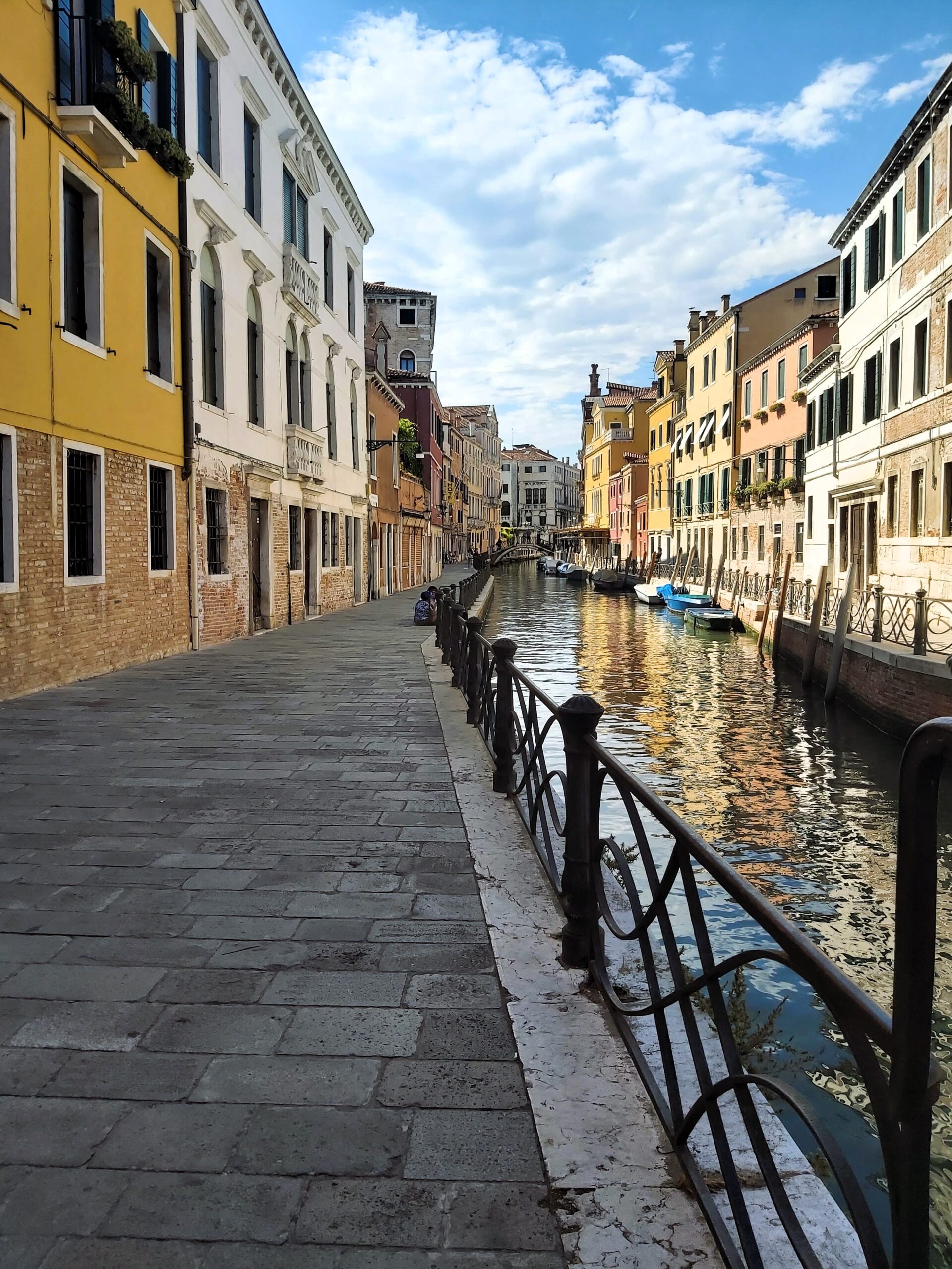 A paved street view alongside a canal with colourful houses in Venice, Italy