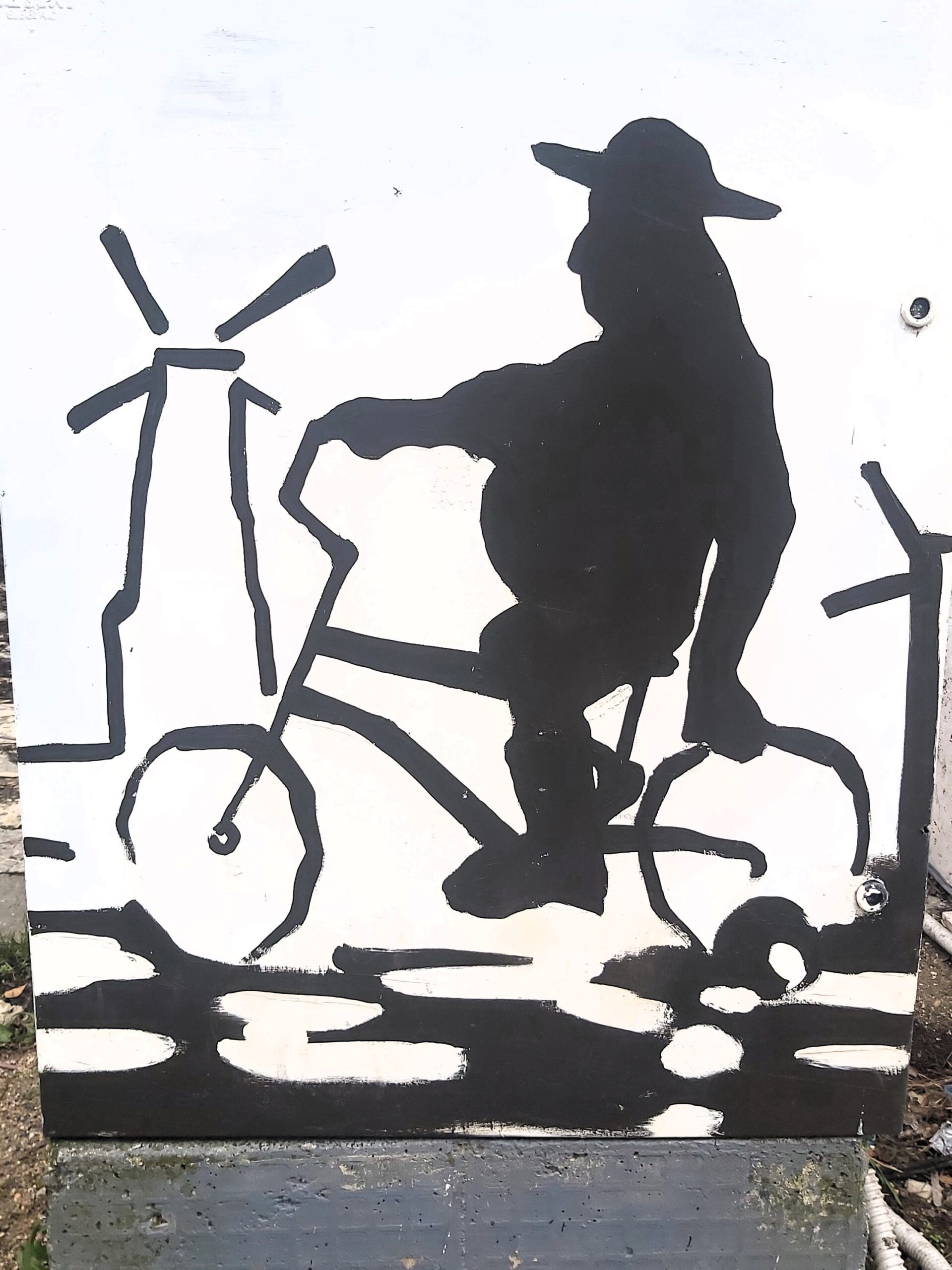 A black and white image of a cyclist and a windmill on a utilities box in Tirana, Albania