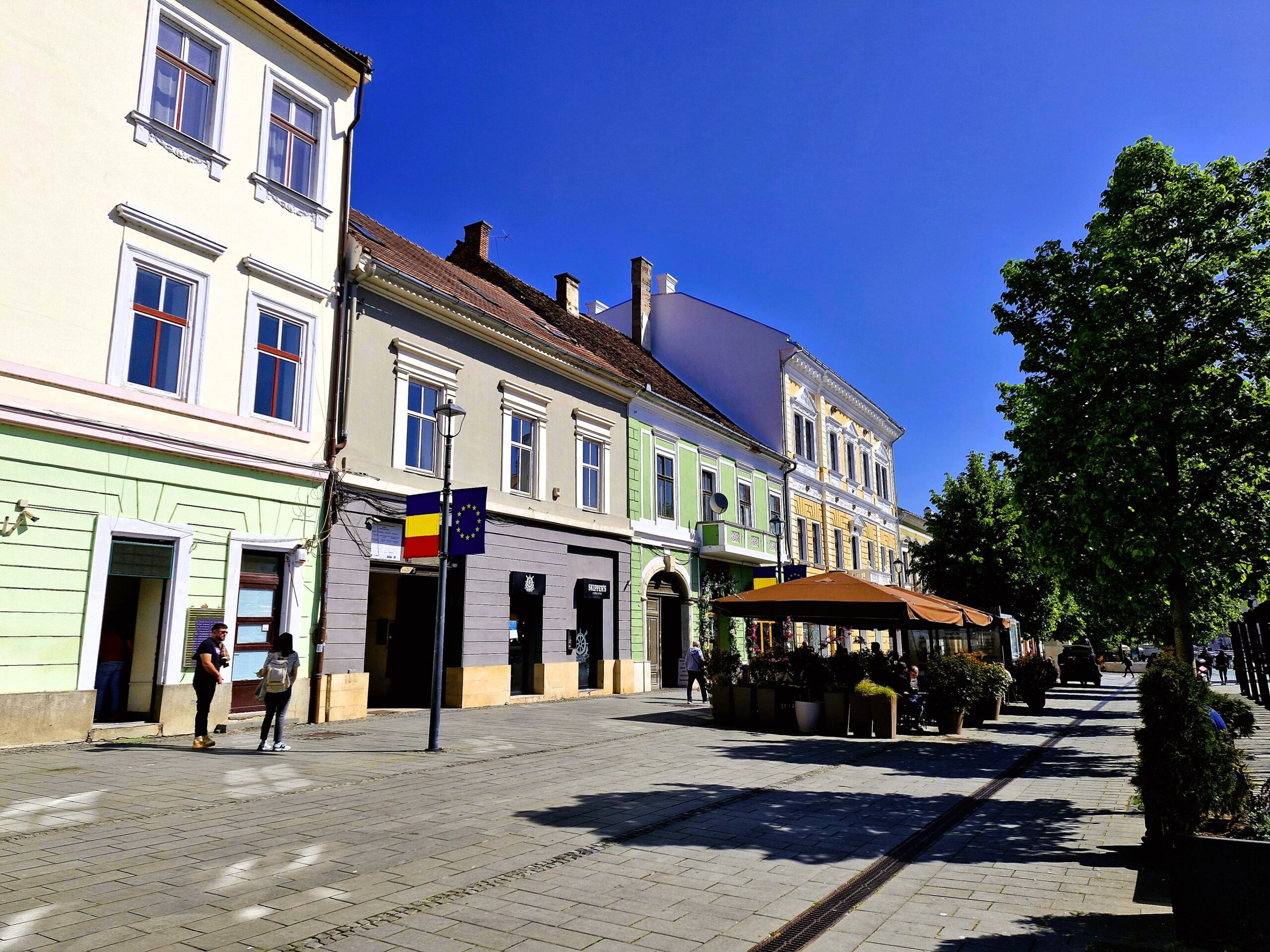 A pretty street scene showing a green, a yellow and a grey building in Cluj-Napoca