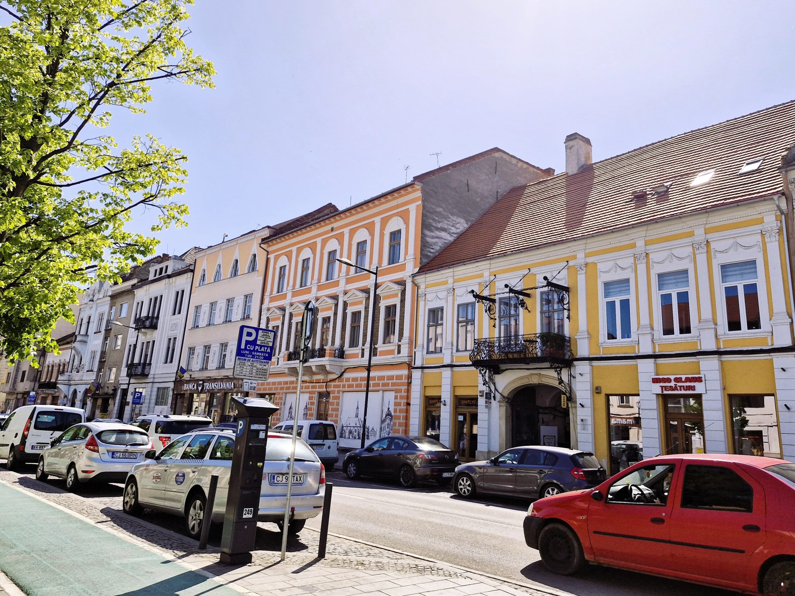 An orange building next to an orange buidling in Cluj-Napoca- both provide a bright pop of colour against the tarmac of the road.
