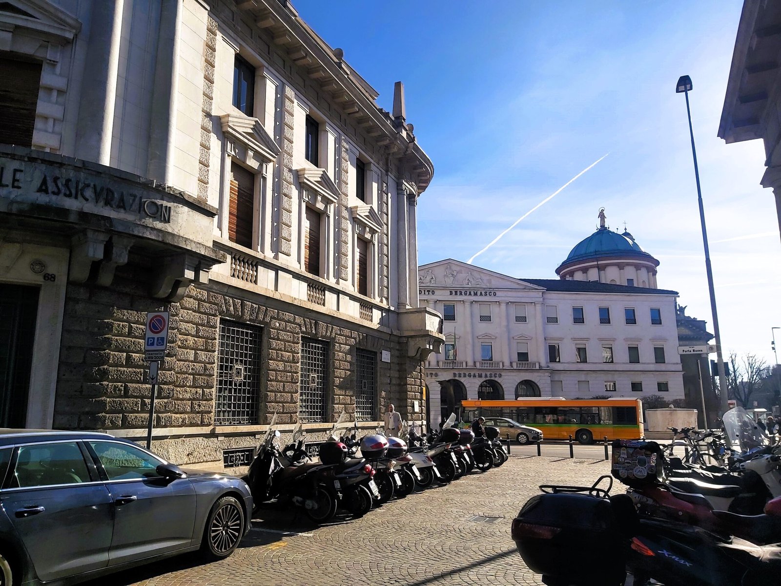 A street scene showing different building styles, motorbikes and vehicles in Bergamo, Italy.